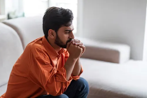Older man sitting quietly with a thoughtful expression, hands folded, in a comfortable home setting.