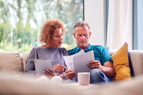 Couple sitting at a kitchen table reviewing documents together, looking relaxed and focused.